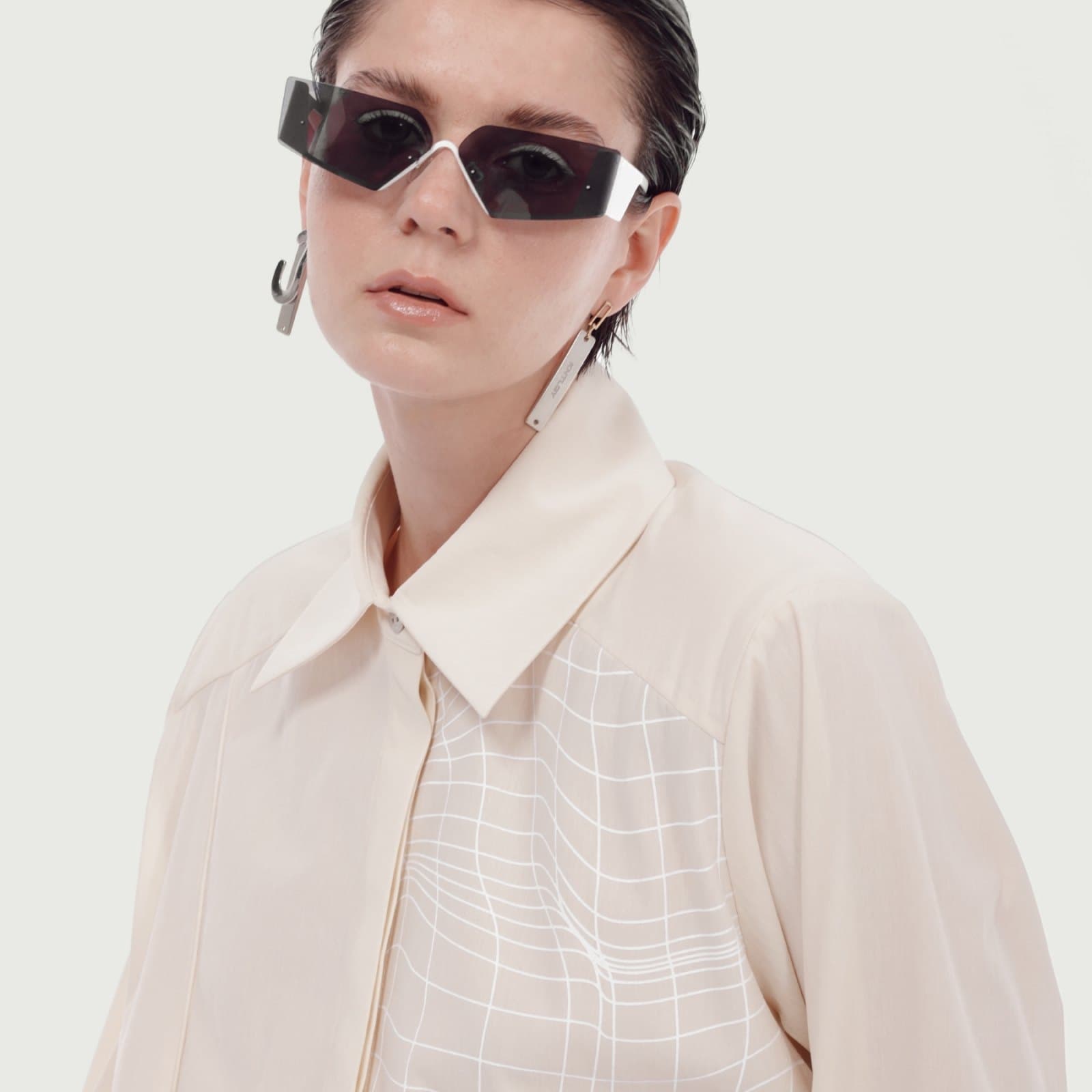 A model in dark glasses wearing a cream shirt with the wireframe print on its front panel